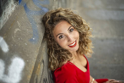 Happy woman with curly hair leaning on wall - BFRF02445