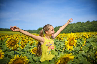 Happy girl with arms outstretched in sunflower field - DIKF00796