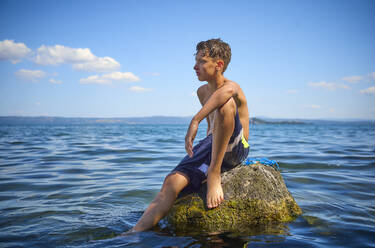 Junge sitzt auf einem Felsen im Bolsena-See, Italien - DIKF00800