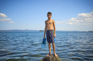 Boy standing on rock in lake Bolsena, Italy - DIKF00803