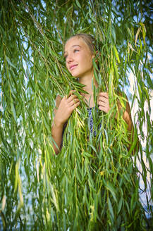 Girl standing amidst leaves of willow tree - DIKF00807