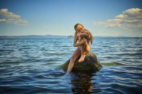 Girl resting on rock in lake Bolsena, Italy - DIKF00809