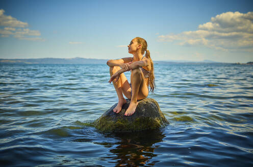 Mädchen sitzt auf einem Felsen im Bolsena-See, Italien - DIKF00810