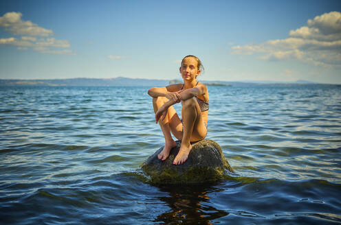 Girl sitting on rock in lake Bolsena, Italy - DIKF00811