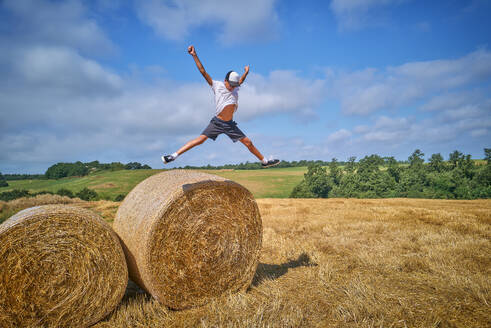 Boy jumping from hay bale on sunny day - DIKF00817