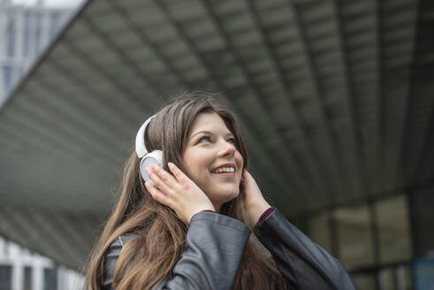 Lächelnde junge Frau, die über drahtlose Kopfhörer Musik hört - BFRF02450