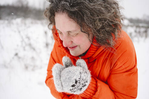 Ältere Frau fröstelt im Schneefeld und trägt Fäustlinge - EYAF02904