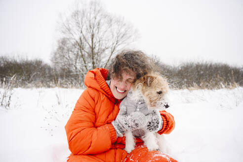 Happy woman embracing dog on snowfield - EYAF02905