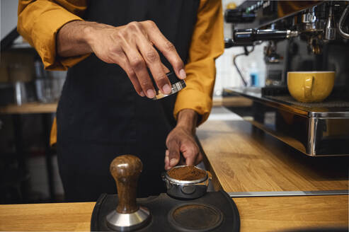 Barista tamping ground coffee in portafilter with tamper at cafe - ALKF00940