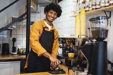 Happy barista tamping ground coffee in portafilter with tamper at cafe - ALKF00941