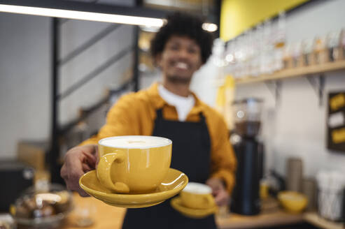 Barista holding yellow coffee cup and saucer - ALKF00948