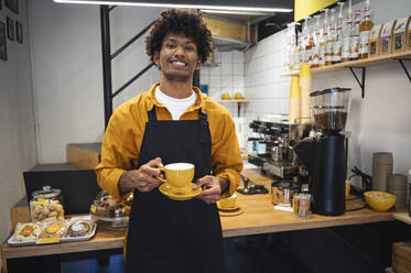 Lächelnder Barista hält eine Tasse Kaffee in der Nähe der Theke - ALKF00949