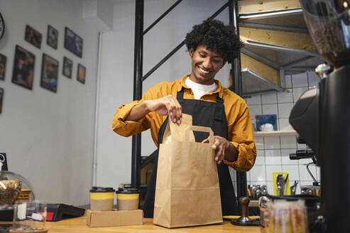 Smiling barista packing takeaway order at coffee shop - ALKF00951