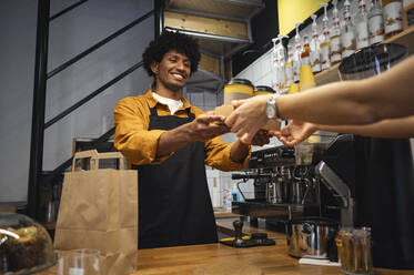 Happy barista handing over takeaway tray to customer at counter in cafe - ALKF00953