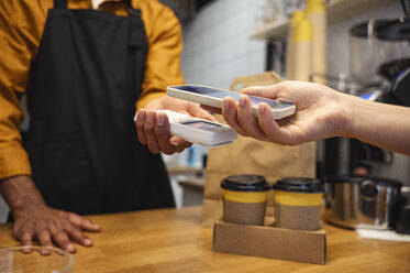 Ein Kunde bezahlt seinen Kaffee mit seinem Smartphone in einem Café - ALKF00954