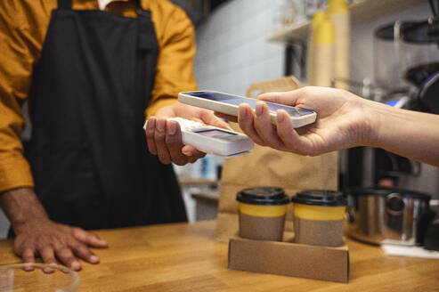 Ein Kunde bezahlt seinen Kaffee mit seinem Smartphone in einem Café - ALKF00954