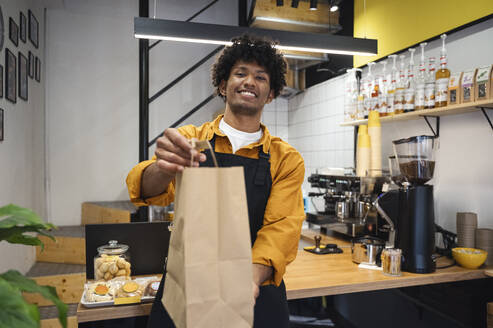 Smiling barista holding takeaway bag at coffee shop - ALKF00957