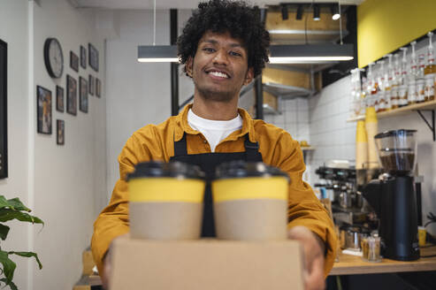 Smiling barista holding takeaway coffee cups at cafe - ALKF00959