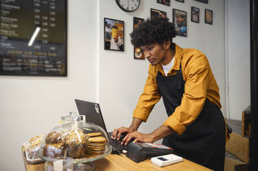 Barista arbeitet am Laptop an der Theke eines Cafés - ALKF00960