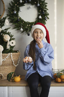 Mädchen mit Weihnachtsmannmütze, das zu Hause Orangen isst - LESF00516