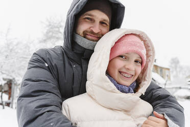 Lächelnder Vater, der seine Tochter im Winter umarmt - EYAF02910