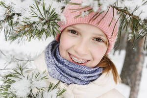 Smiling girl with braces near snow covered tree branches - EYAF02912