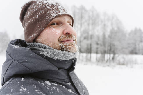 Mature man wearing knitted hat on snowfield - EYAF02916