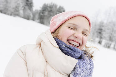 Cheerful girl with eyes closed wearing warm clothes on snowfield - EYAF02917