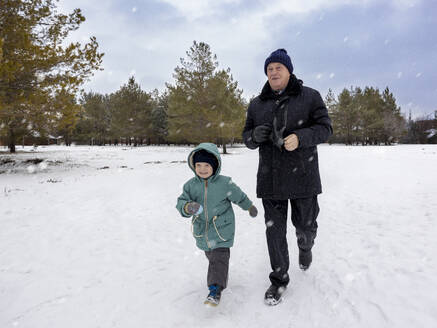 Älterer Mann geht mit Enkel auf Schneefeld spazieren - MBLF00239