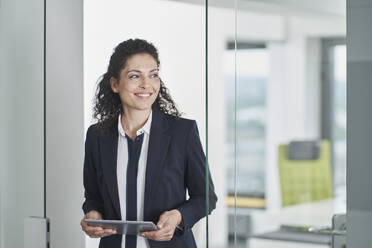 Smiling businesswoman holding tablet PC and standing in office doorway - RORF03675