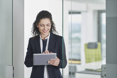 Smiling businesswoman using tablet PC and standing in office doorway - RORF03676