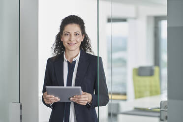 Smiling mature businesswoman standing with tablet PC in office doorway - RORF03678