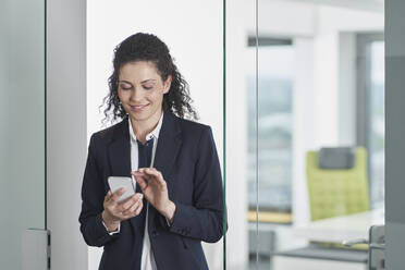 Smiling mature businesswoman using smart phone in office doorway - RORF03681