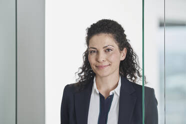 Smiling businesswoman near glass door in office - RORF03684