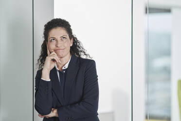 Thoughtful businesswoman leaning on glass door in office - RORF03695