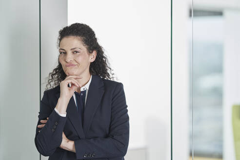 Confused businesswoman with hand on chin standing near glass door - RORF03696