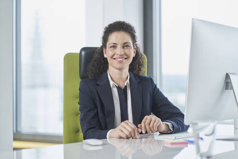 Happy mature businesswoman sitting with computer at desk - RORF03703