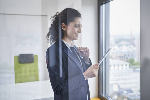 Smiling mature businesswoman using tablet PC seen through glass - RORF03709