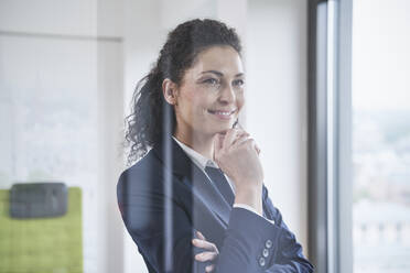 Smiling mature businesswoman with hand on chin seen through glass - RORF03711