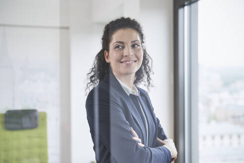 Smiling mature businesswoman with arms crossed seen through glass - RORF03712