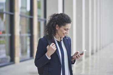 Smiling businesswoman using smart phone near building - RORF03715