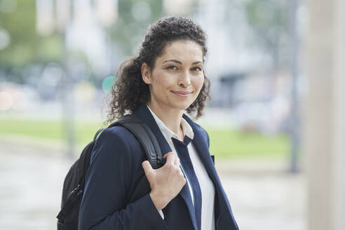 Smiling curly haired businesswoman with backpack - RORF03723