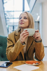 Nachdenkliche Frau in brauner Jacke und mit Kaffee im Café - VSNF01558