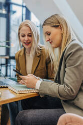 Businesswoman using smart phone with colleague in cafe - VSNF01564