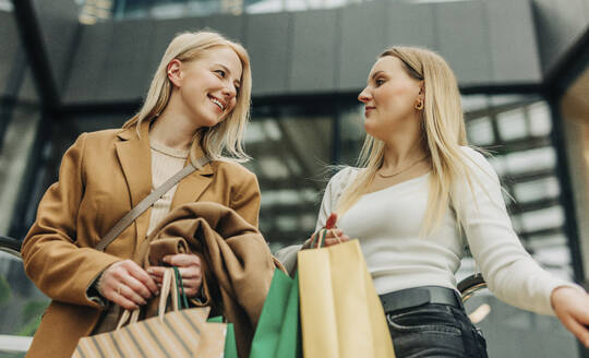 Smiling friends carrying shopping bags in mall - VSNF01568