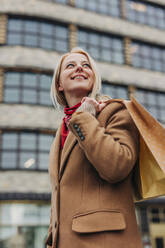 Lächelnde Frau mit Einkaufstüten vor einem Gebäude stehend - VSNF01576