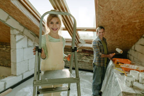Girl standing on ladder near father in room under renovation - YTF01594
