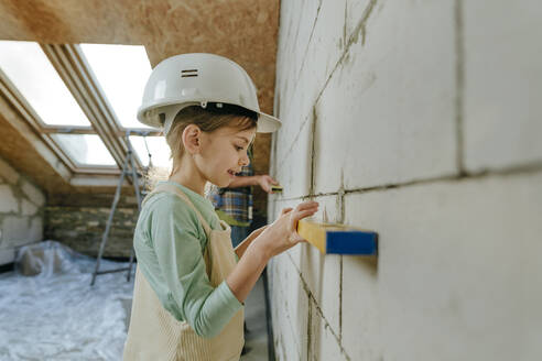 Mädchen mit Nivelliergerät an der Wand in einem zu renovierenden Raum - YTF01607