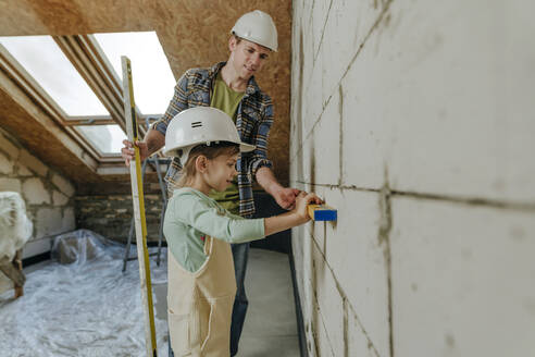 Father and daughter using leveling tool on wall in room under renovation - YTF01608