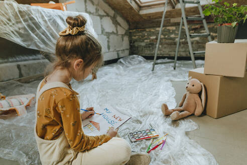 Girl painting house drawing on book sitting with teddy bear at home - YTF01610